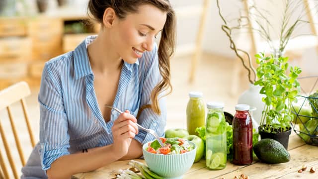 A young, happy woman eating a healthy salad at a table outside