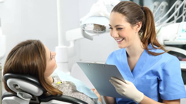 A dentist holding medical chart while talking to a patient in dental clinic