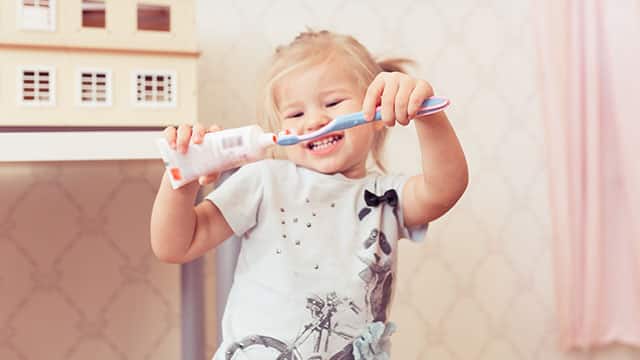 Happy toddler holding toothpaste and a toothbrush smiling