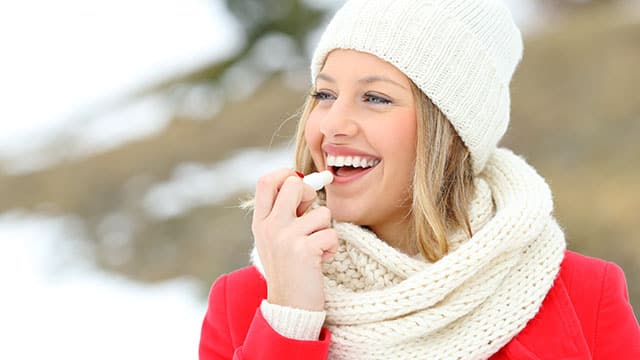Girl applying lip balm on her lips outdoors in the cold