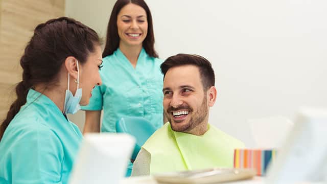 A female dentist, hygienist, and young man smiling in a dentist office 