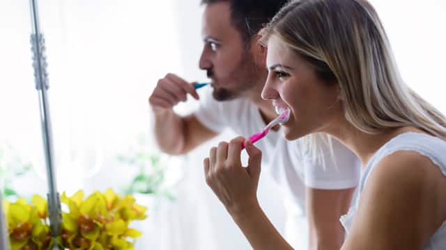 A young couple brushing teeth together while looking in a mirror