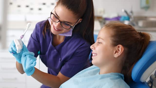 A female dentist in purple scrubs talking with a young female patient
