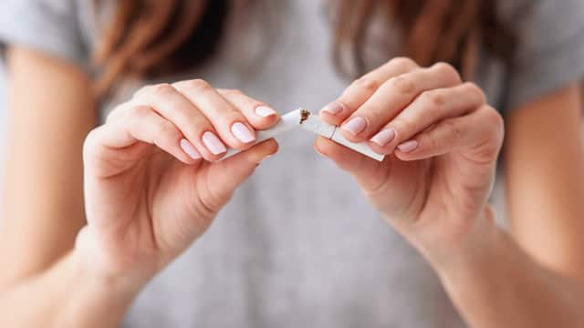 A woman breaking a cigarette in half Close-up of a woman in a gray shirt breaking a cigarette in half