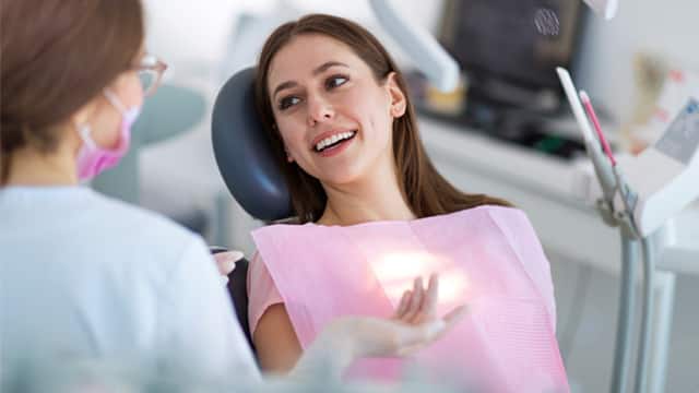 A young woman in a dental chair speaks with a dentist