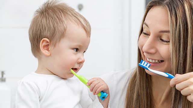 Happy mother teaching her young son how to brush teeth