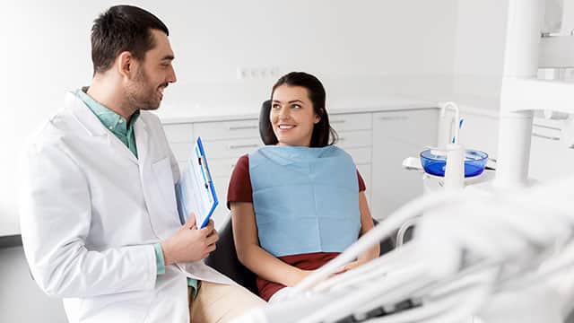 A male dentist with clipboard talking to a female patient and discussing teeth treatment at dental clinic office