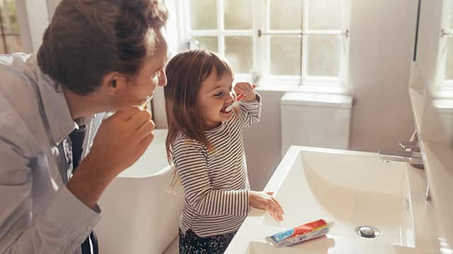 Father teaching daughter how to brush teeth