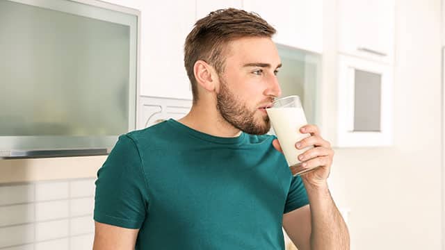 A young man drinking milk from a glass at home