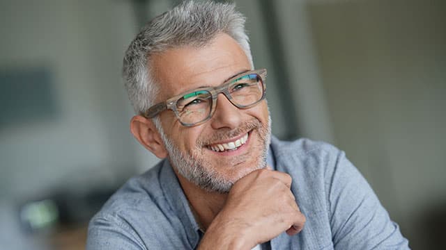 A man wearing glasses is showing his teeth and smiling
