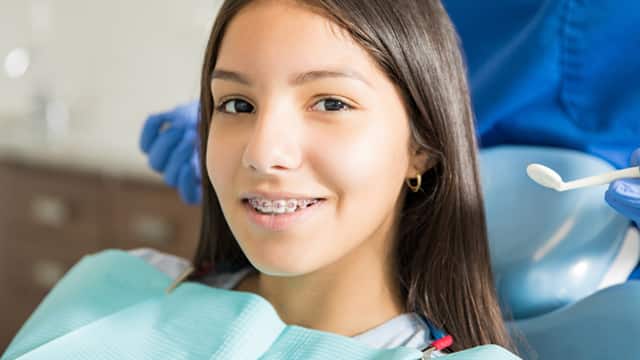 A teenage girl with braces smiling in a dental chair.