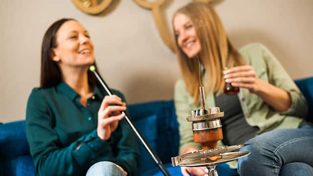 Two happy women are sitting in a bar and smoking hookah