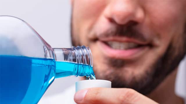  a man is pouring mouthwash into a small cap