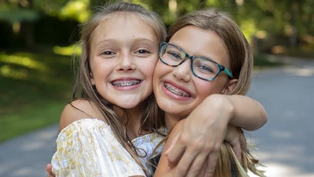 Two tween girls with braces hugging outside