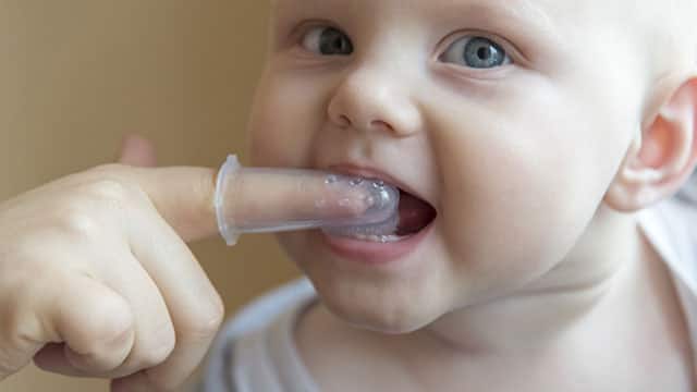 A mom brushes baby's teeth with a brush that fits on her finger