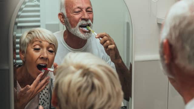 A senior couple brush their teeth in a bathroom mirror