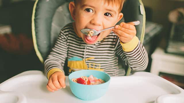 A toddler eating cereal in a highchair