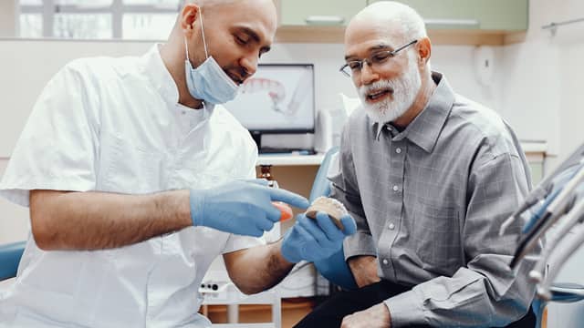 Male dentist discussing dental implants using a model of teeth with a senior male patient