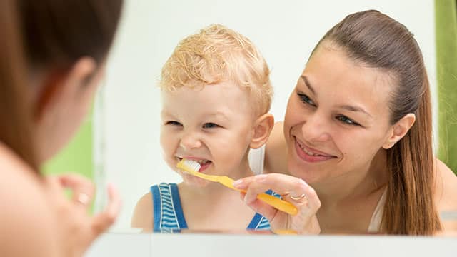 A mother teaching a child teeth brushing in a bathroom