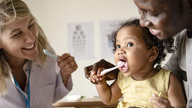 Dentist and parent teaching a little girl how to brush her teeth