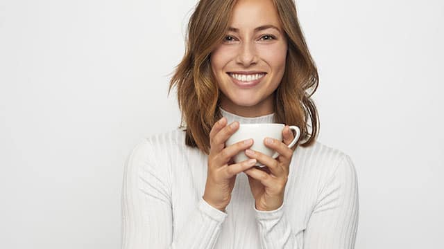 A woman is holding a cup of tea with both hands while smiling
