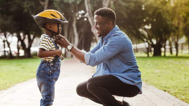 Father putting a bike helmet on his son in a park