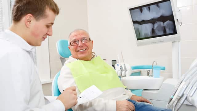 A male dentist talks with a smiling senior man in a dental office