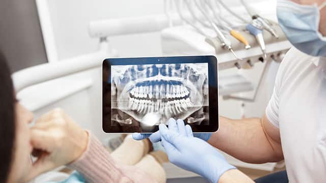 Cropped shot of a professional dentist showing jaws and teeth x-rays to his patient using a digital tablet