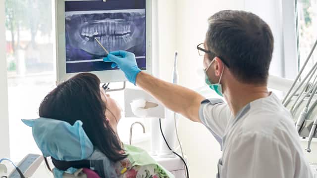 Dentist showing patient's teeth on X-ray while sitting in a dental office