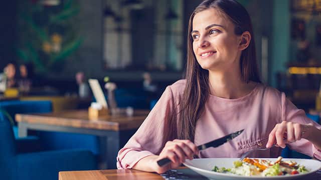 Young woman smiling and looking away while eating lunch at the restaurant