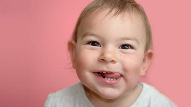 A happy baby toddler smiling and showing teeth and tongue