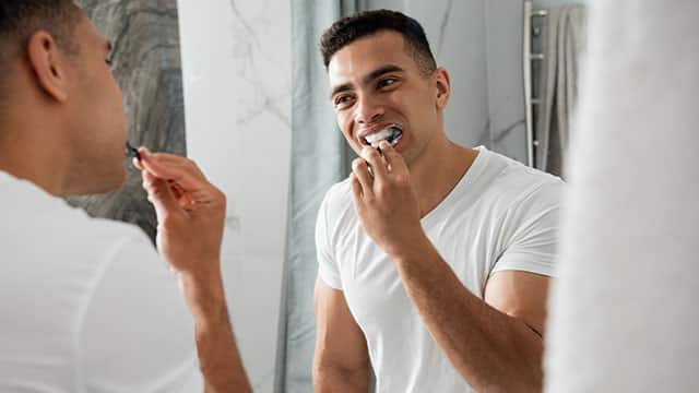 Young smiling man brushing teeth in a bathroom