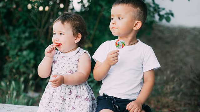 Two children eating candy outdoors in the summer