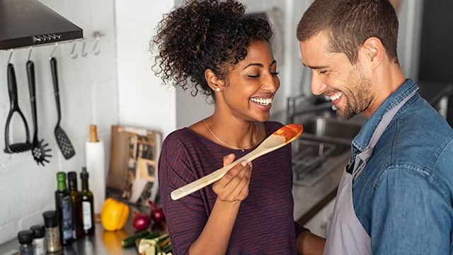 Couple smiling while tasting food in a kitchen