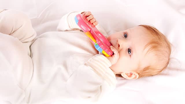 Baby playing with rubber toy in a bed