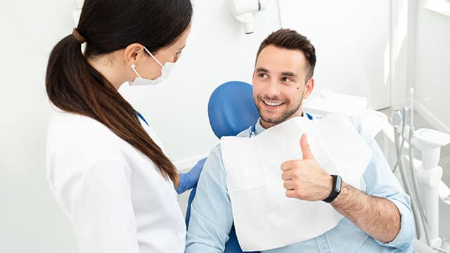 A female dentist and male patient talking as he is showing his thumb up