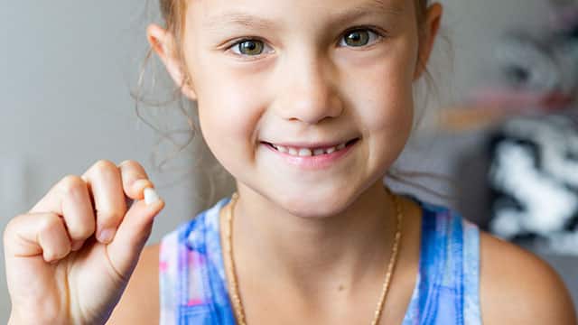 Girl is smiling while holding a tooth that she recently lost 