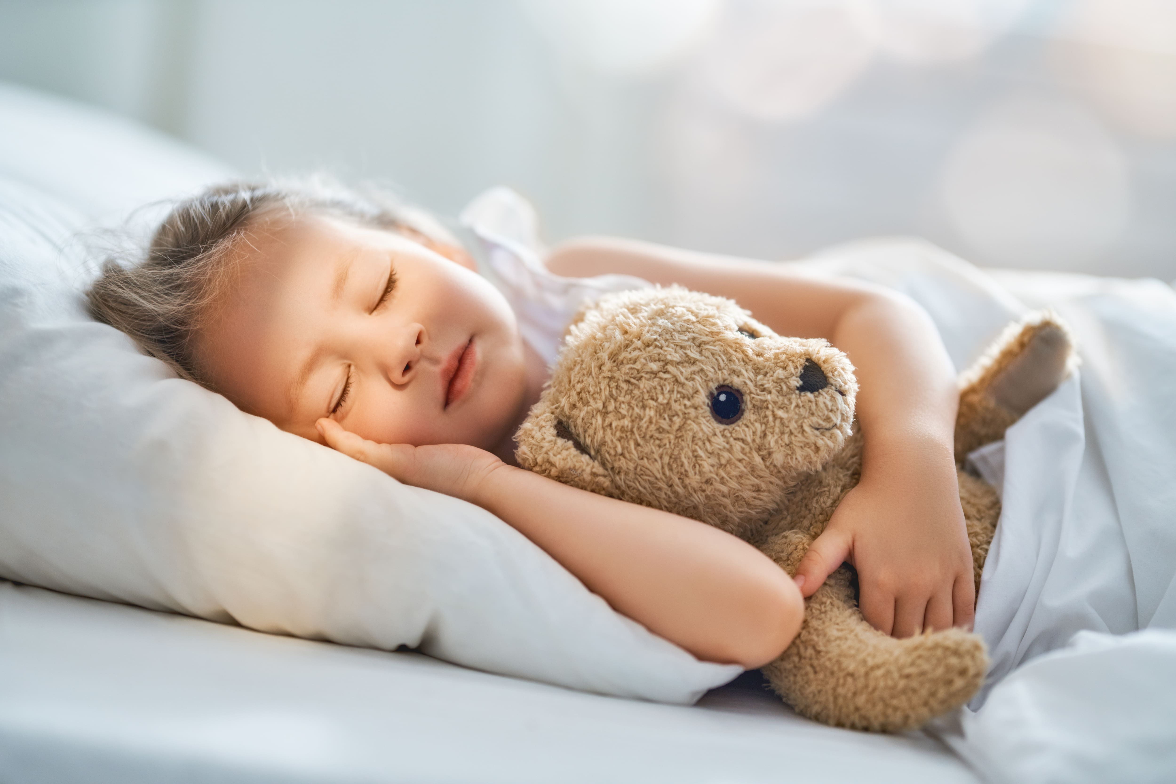 A child girl is sleeping in the bed holding a teddy bear