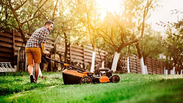 A man is cutting grass and using a lawn mower