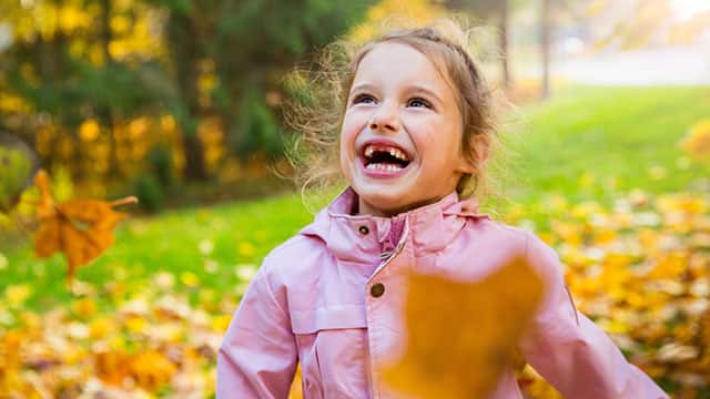A girl with missing teeth playing with yellow fallen leaves in an autumn forest