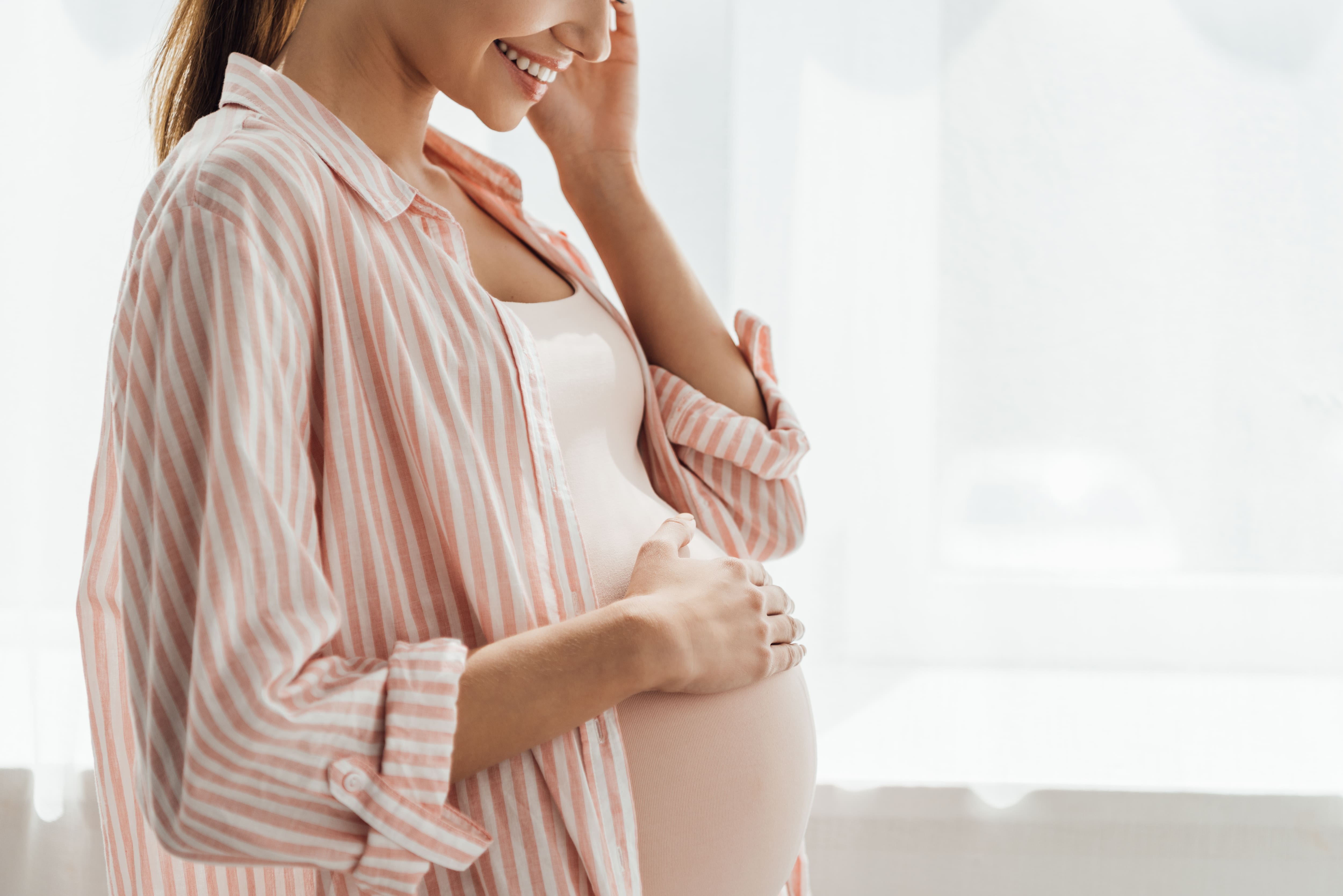 partial view of happy pregnant woman smiling and touching belly