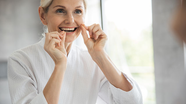 Una mujer de playera blanca usa hilo dental en el baño