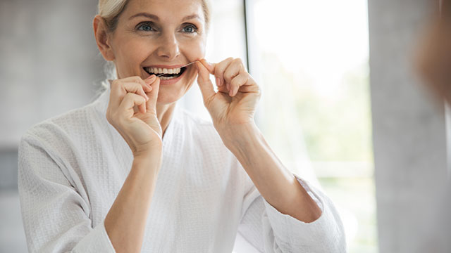 Women using dental floss in a robe in front of the bathroom mirror