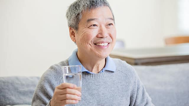 An older man smiling while holding a glass of water 