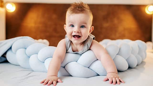 Smiling baby boy lying on stomach on bed in bedroom and looking up
