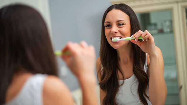 Young woman is brushing her teeth in bathroom.