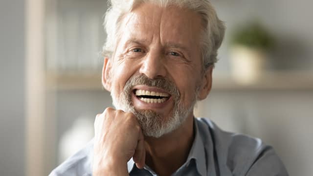 A senior man with gray hair and beard smiling with dentures