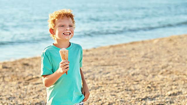 Boy is extremely happy while eating ice cream and smiling at the beach