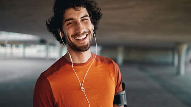 A smiling sporty young man with earphones in his ears looking at camera smiling