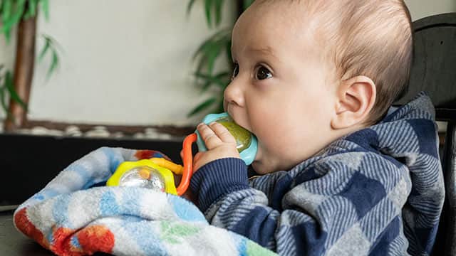 A baby with a blanket is chewing a toy